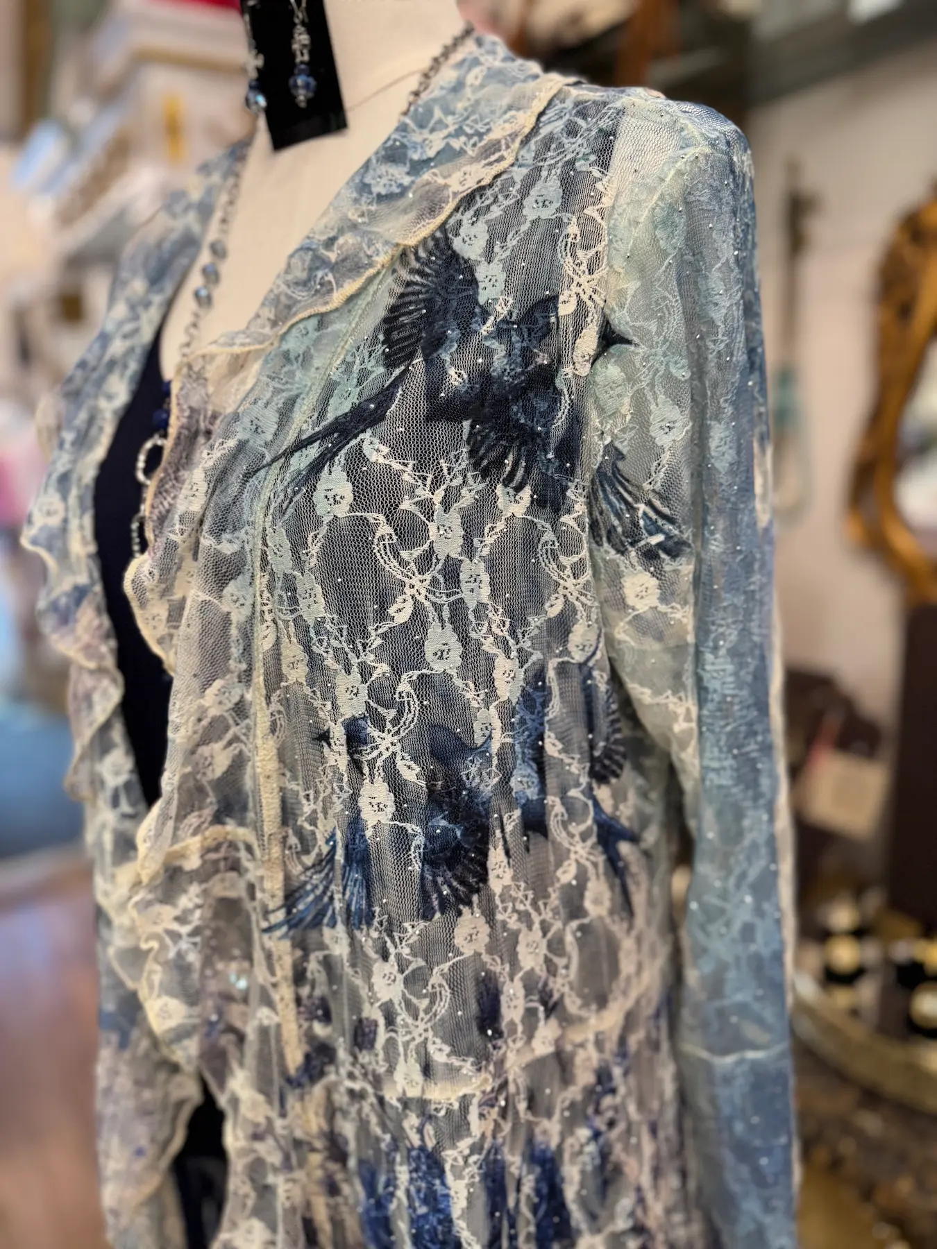 Delicate lace garment with intricate bird embroidery and ruffled edges displayed on a mannequin.